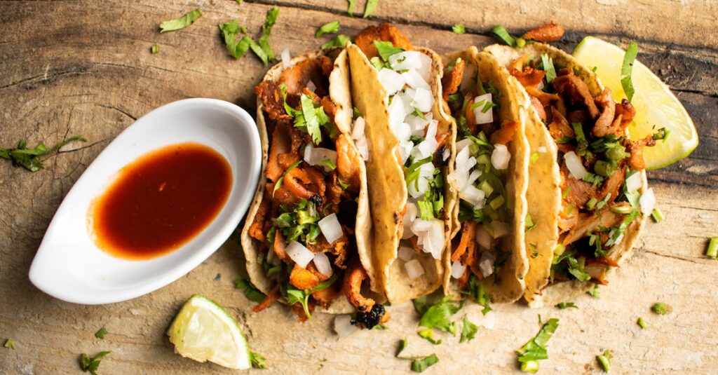 Close-up of three tacos al pastor with cilantro and onion, served with salsa on a rustic table.